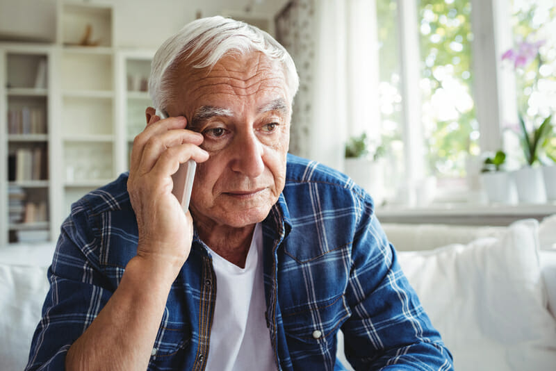 Tensed senior homeowner talking to roofer for roof inspection on mobile phone