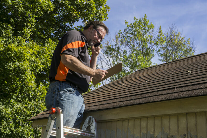 Roofing Contractor On Ladder Figuring Hail Damage Repairs To Roof